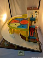 Side angled view showing multi-level garage base, number labeled parking spots, spiral white ramp, yellow supports, and elevator with blue platform.