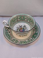 Top-down view of the teacup resting on the matching saucer, showing floral center and green dragon border details.