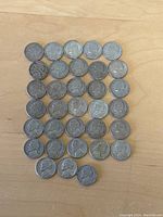 33 Jefferson nickels arranged mostly in grid pattern on wooden surface, showing obverse side with Thomas Jefferson's profile.