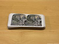 Top view of a stack of 36 WWI stereoscope cards showing a colorized image of soldiers in a rocky battlefield.