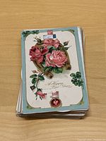 Stack of vintage postcards on wooden surface, front card features pink roses and a New Year greeting.