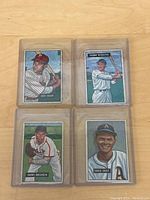 Four 1951 Bowman baseball cards in plastic sleeves laid out on wood surface.