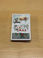 Stack of vintage Christmas postcards with a visible front card showing holly and a winter scene with text 'Wishing you a Merry Xmas'