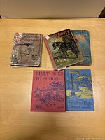 Five children's books arranged on wood surface, showing front covers with visible titles and binding wear.