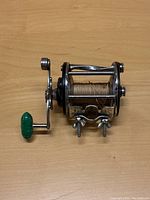 Image showing side and handle of Penn Leveline 350 ocean fishing reel on wooden surface with visible fishing line on spool and green handle grip.
