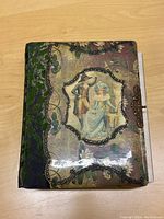 Top view of the vintage photo album showing the detailed cover illustration and velvet decoration.