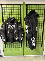 FXR jacket and pants hanging on grid wall