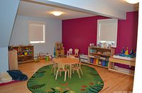 Children’s playroom with freshly painted light gray walls and a single accent wall in magenta, white ceiling and trim, wood-tone flooring, protective coverings along baseboards.
