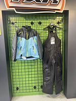 Full view of Arctiva women's snowmobile jacket and bib pants hanging on grid wall