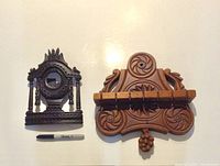 Two hand-carved wooden antique pieces on a white surface with a Sharpie pen for scale: a dark wood pocket watch stand and a lighter wood spoon holder with hooks.