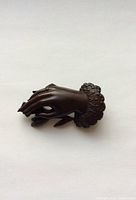Front view of the vulcanite hand-shaped brooch laying flat showing the detailed fingers and floral cuff.