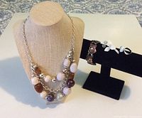 Jewellery set displayed with three-layer necklace on bust and brooch, ring, bracelet on stand