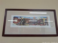 Full view of framed panoramic artwork of Bloor West Village, Toronto, in a dark wood frame with white mat, showing colorful street storefronts and pedestrians.
