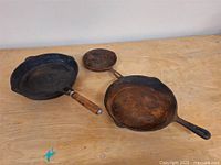Three vintage frying pans on wooden surface showing condition and different sizes