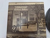 Front cover of the "Tumbleweed Connection" LP by Elton John, depicting a rustic storefront scene in sepia tones.