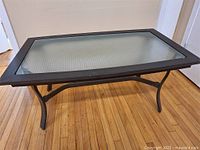 Front and side view of the rectangular coffee table with a black metal frame and tempered glass top on hardwood floor.