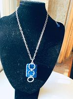 Photo of necklace displayed on black bust showing rectangular sodalite blue pendant with three hammered sterling silver circles, attached to a chain.