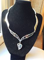 Front view of necklace on black stand showing inlaid onyx and mother of pearl designs and heart-shaped pendant.