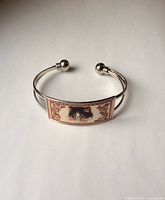 Silver tone metal cat bracelet bangle showing the front view of rectangular plate with cat image on it against a white background.