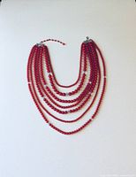 Full view of the seven strand red bead necklace laid flat showing the graduated length of strands and colors.