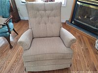 Front facing view of beige upholstered swivel rocker recliner chair showing tufted button backrest, cushioned arms, and padded seat on wood floor.