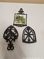 Set of three cast iron trivets on white surface, one with decorative tile insert and two with cut-out iron designs