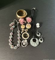 Overview photo of assorted vintage and modern costume jewelry laid flat on black background showing necklaces, earrings, brooches, and bracelet.