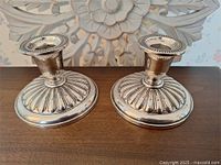 Pair of vintage Birks sterling silver candlesticks shown on a wooden surface in front of a carved floral wall decoration, showing front view with detailed base and candle holder design.