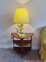 Full view of the wooden corner table and vintage lamp with beige shade lit up, showing water marks on the table surface