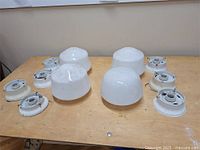 Overview of four white glass light shades alongside six white metal bases on wooden table.