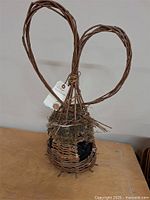 Full view of the willow bird feeder showing woven wicker structure, moss roof, and double-loop handle.