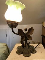 Side view of brass fairy figurine base with flower-shaped frosted glass lampshade lit.