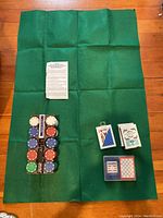 Photo of green felt poker table cover, poker chips in varied colors held in plastic chip holder, four decks of playing cards in different boxes, and instruction sheet.