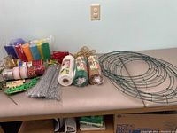 Green metal wreath frames, decorative mesh packages, tulle rolls, wire tinsel stems, assorted ribbons and ties on table
