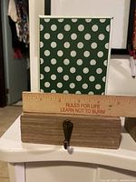 Single wooden stocking holder with a green polka dot backing and metal hook with ruler on top for size reference.