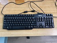 Top view of one Dell wired USB keyboard showing full QWERTY keys, function keys, and numeric keypad on a wood surface.