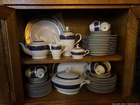Full cabinet view showing stacked plates, bowls, cups, saucers and serving pieces