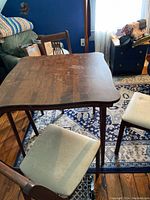 Photo of wooden folding table and two of the matching chairs, showing table surface wear and chair seat cushioning.