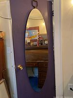 Full length oval mirror hanging on a door, showing reflection and overall shape.