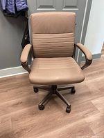 Front view of beige office chair showing padded seat and backrest with horizontal seams and padded armrests on a five-wheel metal base.
