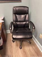 Frontal view of the black high back office chair showing padded seat, backrest, and armrests with rolling casters.