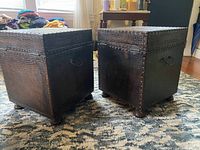 Pair of square wooden trunks with textured exterior and black handles on a patterned carpet.