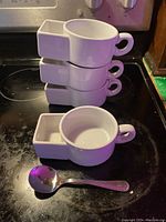 Stack of 4 white ceramic soup and cracker bowls with a spoon for size comparison on a black stovetop.