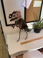 Side view of welded metal T. rex sculpture on white table with ruler for scale.