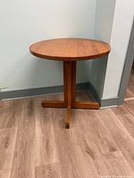 Side view of one wooden bistro table showing round top and four-foot pedestal base.