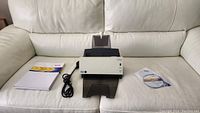 Scanner with power cord, software CD, and manuals placed on white couch