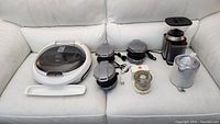 Full lot overview on white couch showing all items including large George Foreman grill, 3 sandwich makers, food processor, coffee grinder and citrus juicer