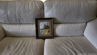 Photo of the framed watercolor painting placed on a tan leather couch, showing the full frame and painting size.