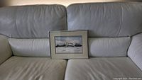 Full view of the framed watercolor painting on a gray couch, showing overall condition and size