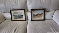 Both framed watercolor paintings displayed side by side on a light-colored couch